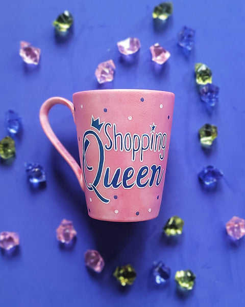 a shimmery pink hand paitned mug with teh words shopping queen written in white a shimmery blue. with blue and white dots scattered all over the mug