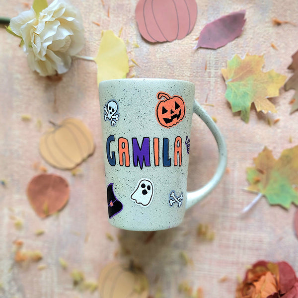 An Ivory hand painted mug with the name "gamila" and Halloween items and black dots scattered all over