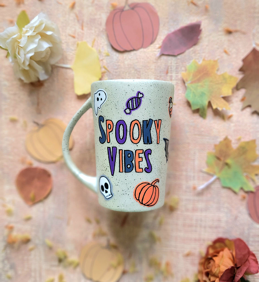 An Ivory Hand painted mug with the words "Spooky Vibes" and Halloween items and black dots scattered all over