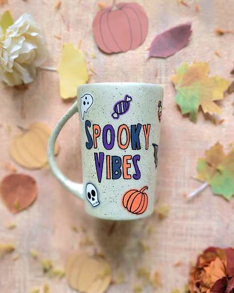 An Ivory Hand painted mug with the words "Spooky Vibes" and Halloween items and black dots scattered all over