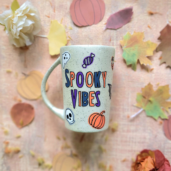 An Ivory Hand painted mug with the words "Spooky Vibes" and Halloween items and black dots scattered all over