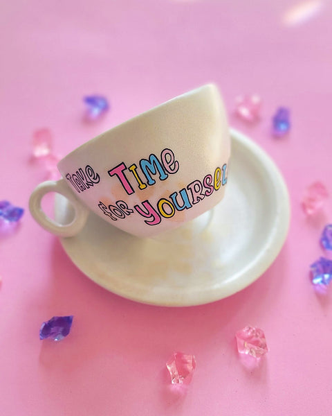 A Pearl white hand painted cup and saucer with gold geomteric patterns in the background and the words "Take time for Yourself"