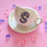 A Pearl white hand painted mug with gold geomteric patterns in the background and the letter S