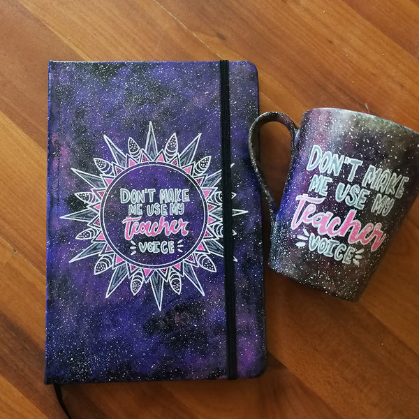 A Gift Set of a mug and matching notebook both hand painted in black galaxy color and have the sentence "don't make me use my teacher voice"