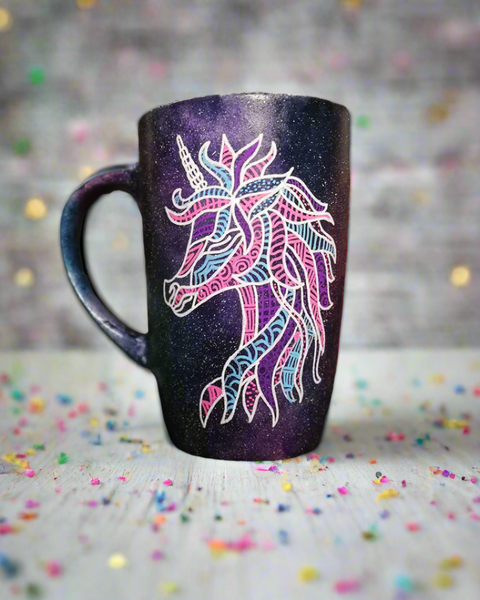 A black galaxy hand painted mug with a zentangle unicorn design on it