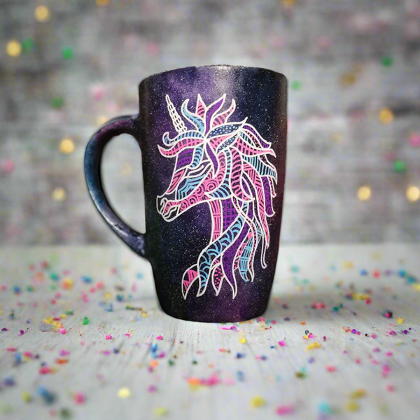 A black galaxy hand painted mug with a zentangle unicorn design on it