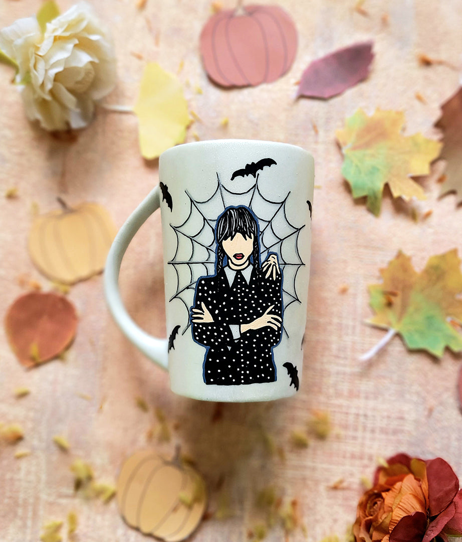 An Ivory hand painted mug with a gothic girl drawn in the center and a web behind her with bats all over the mug