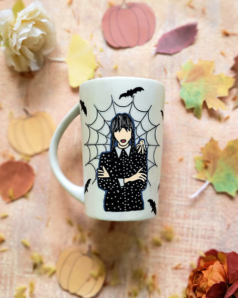 An Ivory hand painted mug with a gothic girl drawn in the center and a web behind her with bats all over the mug