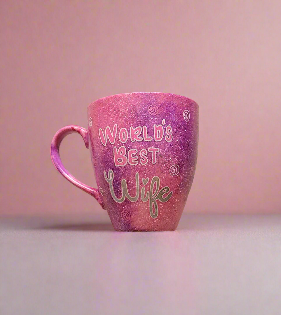 A Hand painted pink galaxy mug with the sentence " worlds best wife" and small swirls all over the mug