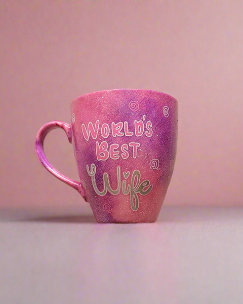 A Hand painted pink galaxy mug with the sentence " worlds best wife" and small swirls all over the mug